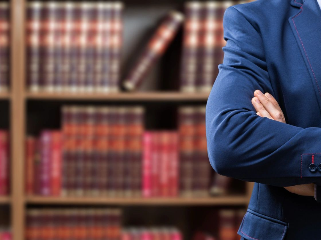 expert witness torso side of person in blue suit with bookshelf and books in the background