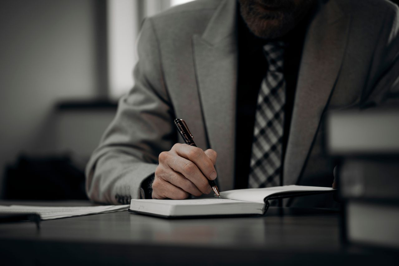 expert-witness-taking-notes expert witness at a desk taking notes on a bound notebook